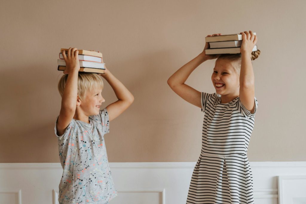 Two children holding stacks of books on their heads.